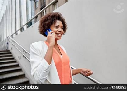 business, communication, technology and people concept - young smiling african american businesswoman calling on smartphone going down stairs into city underpass