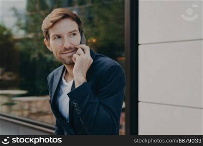 Business communication. Young handsome urban professional businessman listening to customer on cell phone, discussing something on smartphone, standing alone next to building with reflective window. Handsome urban professional businessman listening to customer on cell phone while standing outside