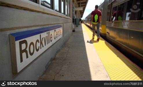 Business commuter at Rockville Centre train passing the station sign