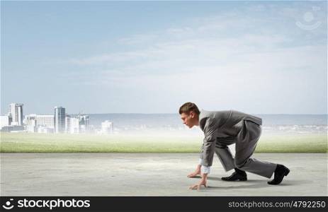 Business competition. Side view of young businessman in start position ready to run