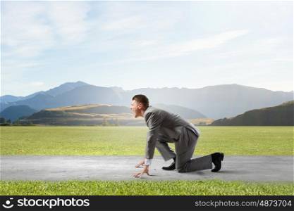 Business competition. Side view of young businessman in start position ready to run