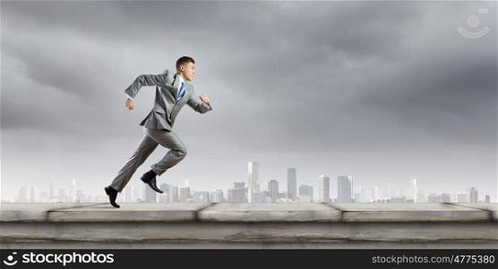 Business competition. Young businessman in suit running on road