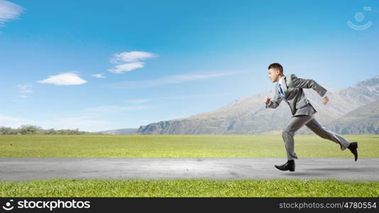 Business competition. Young businessman in suit running on road