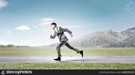 Business competition. Young businessman in suit running on road