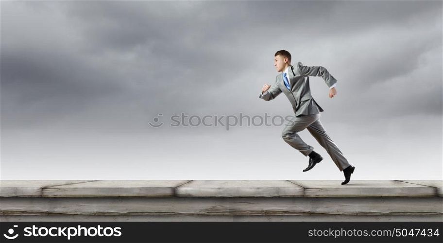 Business competition. Young businessman in suit running on road