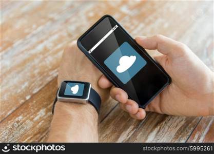 business, computing, technology and people concept - close up of male hand holding smart phone and wearing watch with cloud icon on screen at home