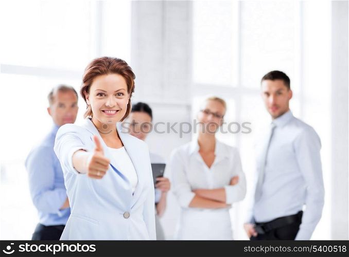business concept - attractive businesswoman with team in office showing thumbs up