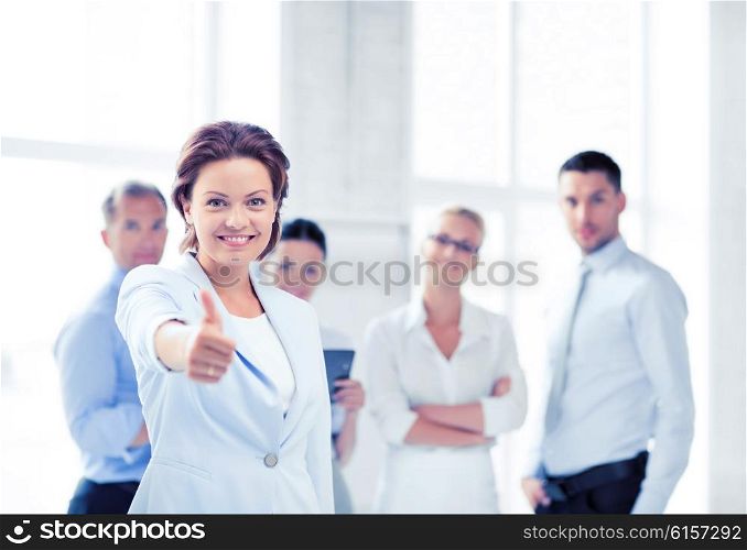 business concept - attractive businesswoman with team in office showing thumbs up. businesswoman in office showing thumbs up