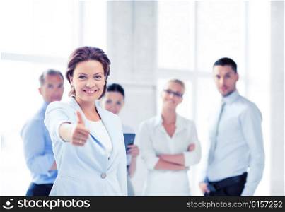 business concept - attractive businesswoman with team in office showing thumbs up. businesswoman in office showing thumbs up
