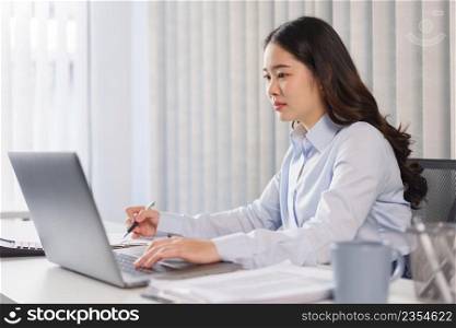 Business concept, Businesswoman checking financial data on laptop and taking notes on document.