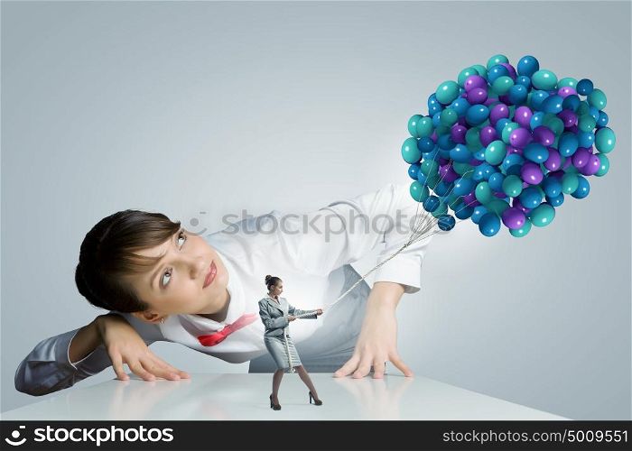 Business concept. Businesswoman looking at businesswoman miniature pulling bunch of balloons