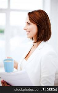 business concept - businesswoman with cup of coffee and papers in office