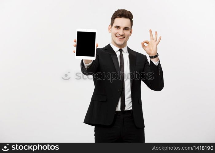 Business Concept: Cheerful businessman in smart suit with pc tablet showing ok. Isolated over grey background. Business Concept: Cheerful businessman in smart suit with pc tablet showing ok. Isolated over grey background.