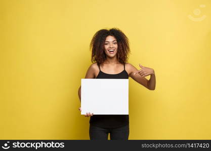 Business Concept - Close up Portrait young beautiful attractive African American pointing finger to plain white blank sign. Yellow Pastel studio Background. Copy space.. Business Concept - Close up Portrait young beautiful attractive African American pointing finger to plain white blank sign. Yellow Pastel studio Background. Copy space