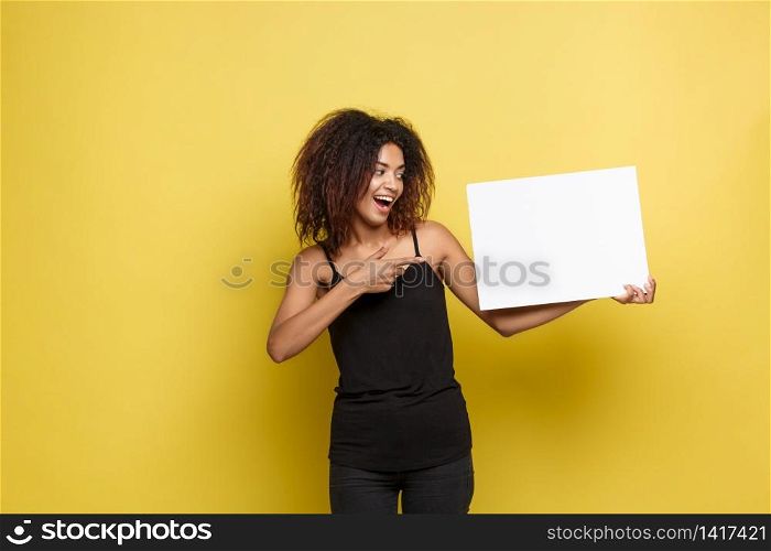 Business Concept - Close up Portrait young beautiful attractive African American pointing finger to plain white blank sign. Yellow Pastel studio Background. Copy space.. Business Concept - Close up Portrait young beautiful attractive African American pointing finger to plain white blank sign. Yellow Pastel studio Background. Copy space