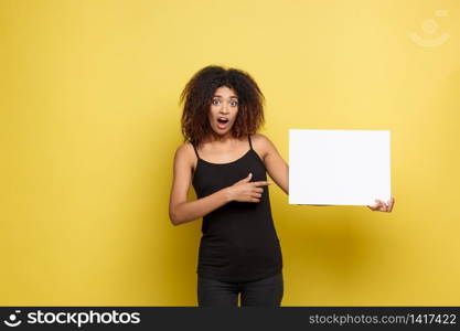 Business Concept - Close up Portrait young beautiful attractive African American pointing finger to plain white blank sign. Yellow Pastel studio Background. Copy space.. Business Concept - Close up Portrait young beautiful attractive African American pointing finger to plain white blank sign. Yellow Pastel studio Background. Copy space