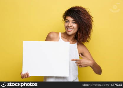 Business Concept - Close up Portrait young beautiful attractive African American pointing finger to plain white blank sign. Yellow Pastel studio Background. Copy space.. Business Concept - Close up Portrait young beautiful attractive African American pointing finger to plain white blank sign. Yellow Pastel studio Background. Copy space