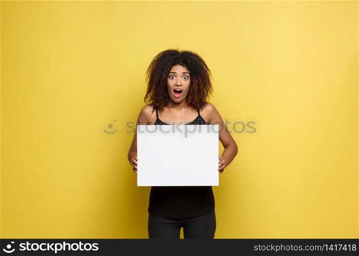 Business Concept - Close up Portrait young beautiful attractive African American shocking expression showing plain white blank sign. Yellow Pastel studio Background. Copy space.. Business Concept - Close up Portrait young beautiful attractive African American shocking expression showing plain white blank sign. Yellow Pastel studio Background. Copy space