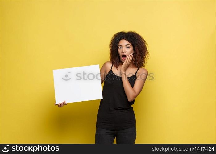 Business Concept - Close up Portrait young beautiful attractive African American smiling showing plain white blank sign. Yellow Pastel studio Background. Copy space.. Business Concept - Close up Portrait young beautiful attractive African American smiling showing plain white blank sign. Yellow Pastel studio Background. Copy space
