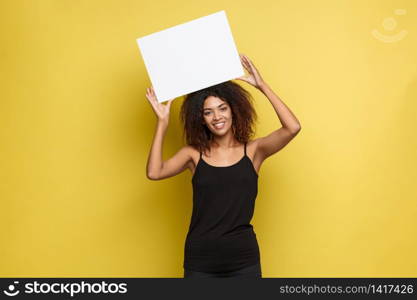 Business Concept - Close up Portrait young beautiful attractive African American smiling showing plain white blank sign. Yellow Pastel studio Background. Copy space.. Business Concept - Close up Portrait young beautiful attractive African American smiling showing plain white blank sign. Yellow Pastel studio Background. Copy space