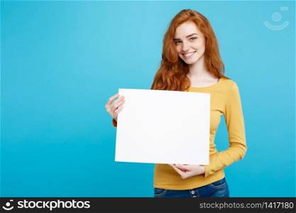 Business Concept -Close up Portrait young beautiful attractive ginger red hair girl smiling showing blank sign. Blue Pastel Background. Copy space.