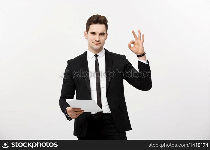 Business Concept: Portrait attractive businessman working on report and showing ok finger sign. Isolated over grey copy space. Business Concept: Portrait attractive businessman working on report and showing ok finger sign. Isolated over grey copy space.