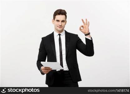 Business Concept: Portrait attractive businessman working on report and showing ok finger sign. Isolated over grey copy space. Business Concept: Portrait attractive businessman working on report and showing ok finger sign. Isolated over grey copy space.