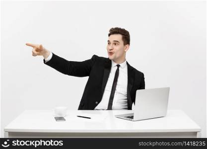 Business Concept: Portrait of handsome businessman dressed in suit sitting in office pointing finger at copy space and laptop isolated over gray background.. Business Concept: Portrait of handsome businessman dressed in suit sitting in office pointing finger at copy space and laptop isolated over gray background
