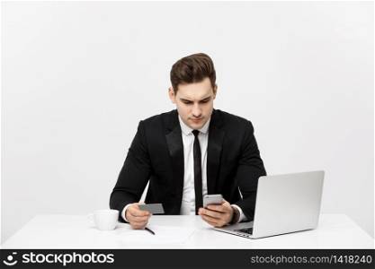 Business Concept: Portrait of young businessman using laptop computer and mobile phone holding debit card. Isolated over grey background. Business Concept: Portrait of young businessman using laptop computer and mobile phone holding debit card. Isolated over grey background.