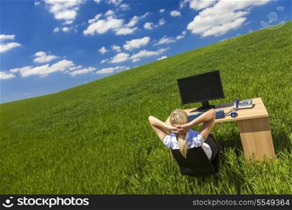 Business concept shot of a beautiful young woman or businesswoman relaxing at a desk with computer in a green field with a bright blue sky.