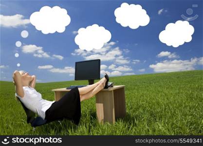 Business concept shot of a beautiful young woman relaxing at a desk in a green field day dreaming, white dream clouds in a blue sky.