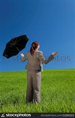 Business concept shot of a beautiful young woman standing in a green field under a bright blue sky holding and umbrella and looking towards the light. Shot on location.