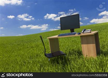 Business concept shot showing a computer on a desk in a green field with a blue sky and white clouds
