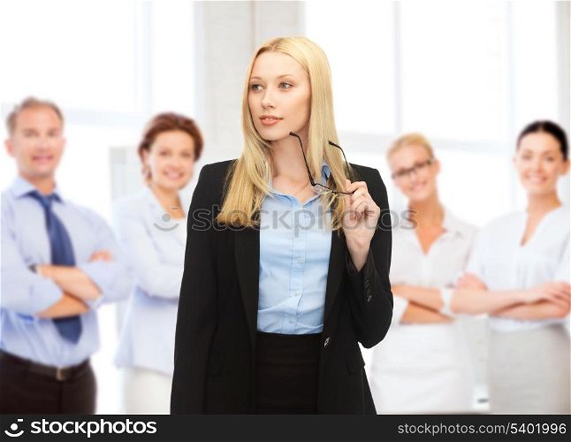business concept - smiling businesswoman with eyeglasses and team behind