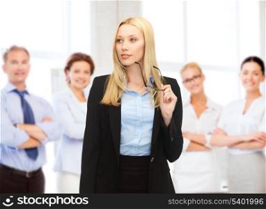 business concept - smiling businesswoman with eyeglasses and team behind