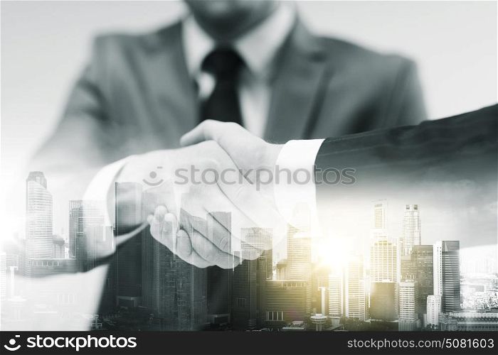 business, cooperation, partnership and people concept - two businessmen shaking hands at office over city buildings and double exposure effect. two businessmen shaking hands at office