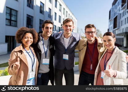 business, corporate and success concept - international group of people with name tags or conference badges showing thumbs up on city street. business team with conference badges in city