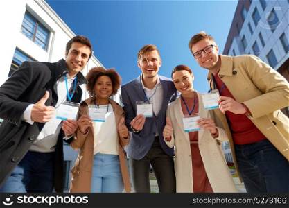 business, corporate and success concept - international group of people with name tags or conference badges showing thumbs up on city street. business team with conference badges in city