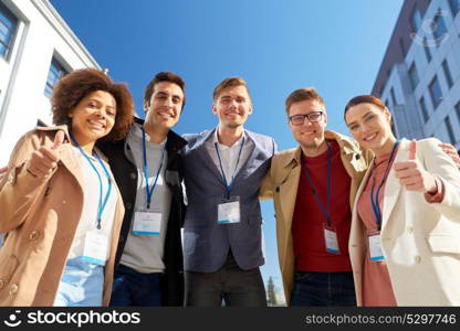 business, corporate and success concept - international group of people with name tags or conference badges showing thumbs up on city street. business team with conference badges in city