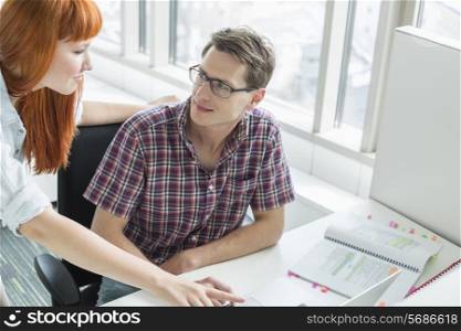 Business couple looking at each other while using laptop in creative office