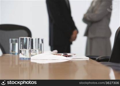 Business couple standing by conference table, mid section, focus on table