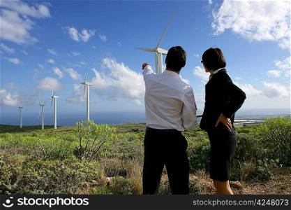Business couple standing in a field of wind turbines