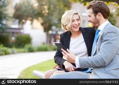 Business Couple Using Digital Tablet On Park Bench