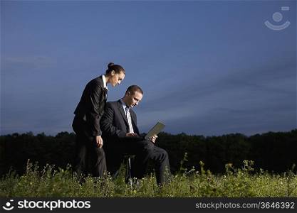 Business couple using laptop in field