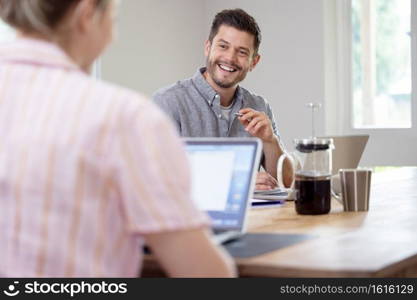 Business Couple Working From Home Sitting At Table During Pandemic Lockdown