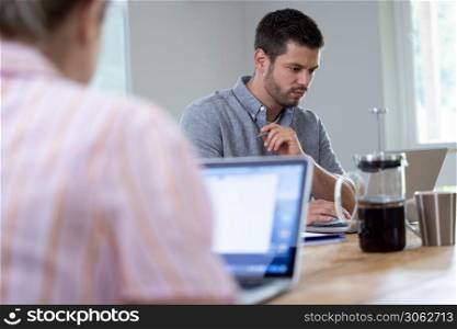 Business Couple Working From Home Sitting At Table During Pandemic Lockdown