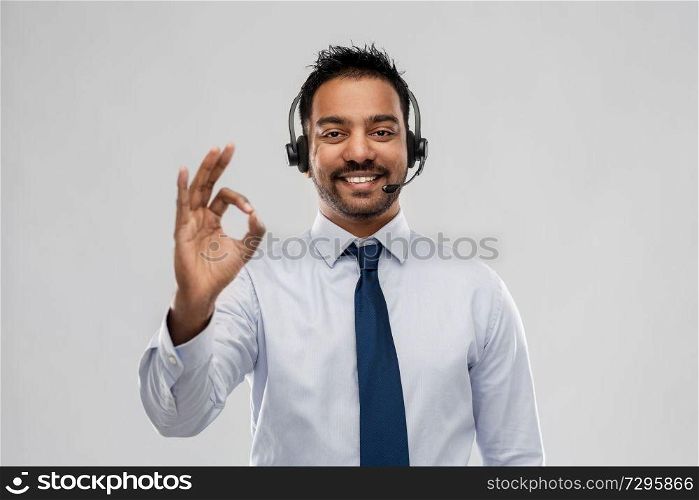 business, customer service and people concept - smiling indian businessman or helpline operator in headset over grey background showing ok gesture. businessman or helpline operator showing ok sign
