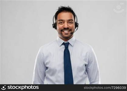 business, customer service and people concept - smiling indian businessman or helpline operator in headset over grey background. indian businessman or helpline operator in headset