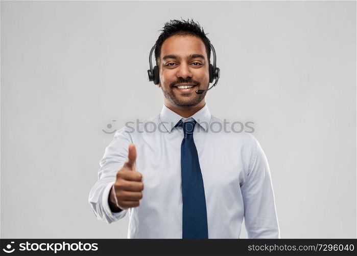 business, customer service and people concept - smiling indian businessman or helpline operator in headset showing thumbs up over grey background. businessman or helpline operator showing thumbs up
