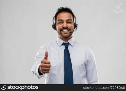 business, customer service and people concept - smiling indian businessman or helpline operator in headset showing thumbs up over grey background. businessman or helpline operator showing thumbs up